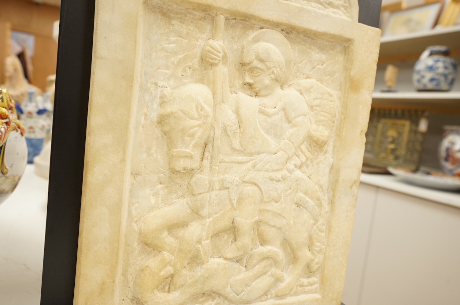 A 19th century carved white marble panel depicting Saint George and the dragon, on stand, 37cm
